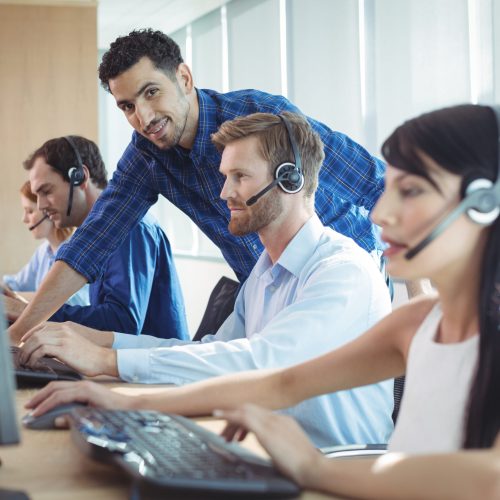 Smiling male supervisor assisting telemarketer at desk in call center