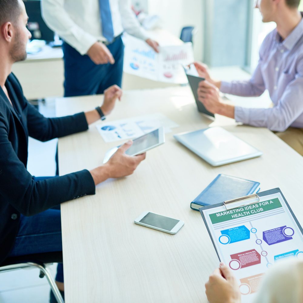 High angle view at meeting table with group of people sitting around it in board room listening to marketing presentation